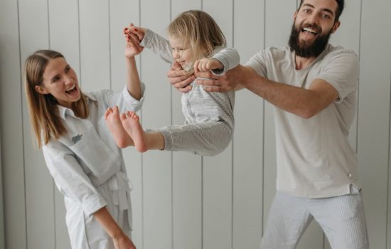 Joyful parents playing with their daughter indoors, all wearing white, capturing a moment of happiness.