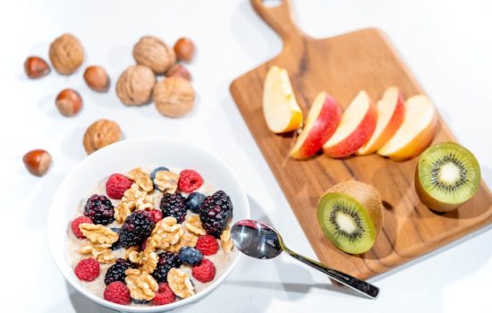 A nutritious breakfast bowl featuring fresh berries and walnuts, served with sliced fruit and kiwi.